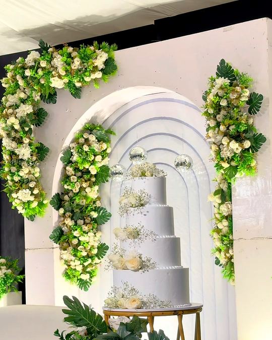 Tiered white wedding cake inside a sculpted arch of white florals