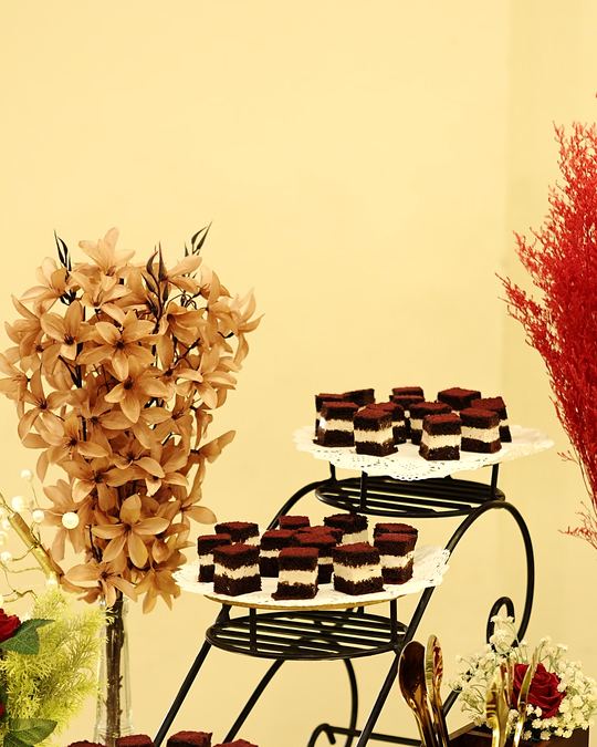 Red velvet cupcakes on a gold tiered stand beside a dried-flower arrangement