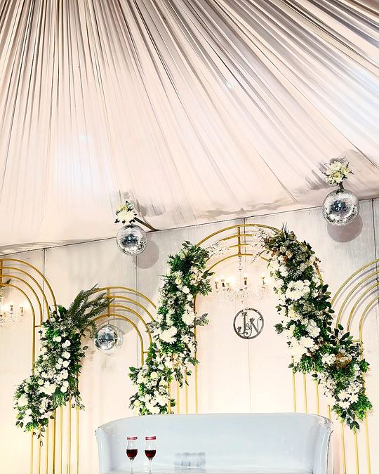 White stage with gold arches, greenery and a white sofa